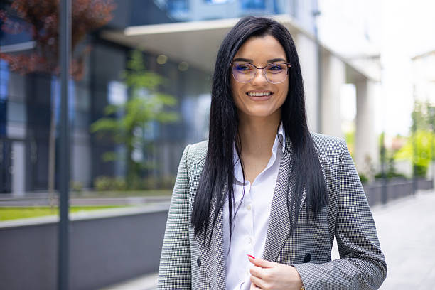 istock Young businesswoman wearing glasses smiling, feeling confident and successful while standing outside modern office building 2249695383