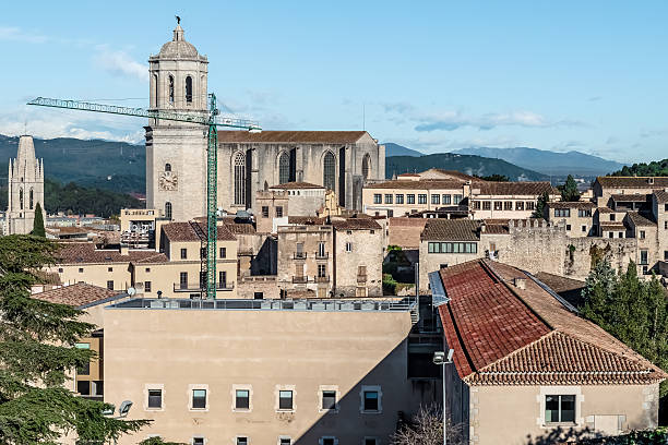 Panoramic view of Girona Cathedral dominating the cityscape with its Gothic architecture. Construction crane visible near the cathedral with Pyrenees mountains in the background. Historic buildings of Girona, Catalonia, Spain