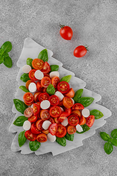 istock Festive Christmas Caprese salad with cherry tomatoes, mini mozzarella, and fresh basil served on a marble board, styled in the shape of a Christmas tree for holiday celebrations. Top view. 2249701832