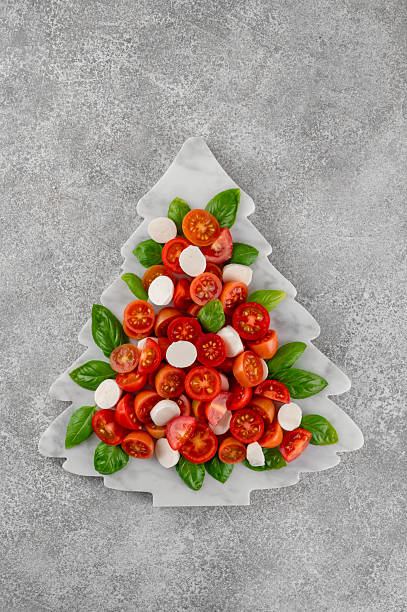 istock Festive Christmas Caprese salad with cherry tomatoes, mini mozzarella, and fresh basil served on a marble board, styled in the shape of a Christmas tree for holiday celebrations. Top view. 2249701834