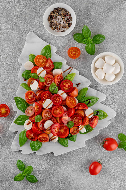 istock Festive Christmas Caprese salad with cherry tomatoes, mini mozzarella, and fresh basil served on a marble board, styled in the shape of a Christmas tree for holiday celebrations. Top view. 2249701853