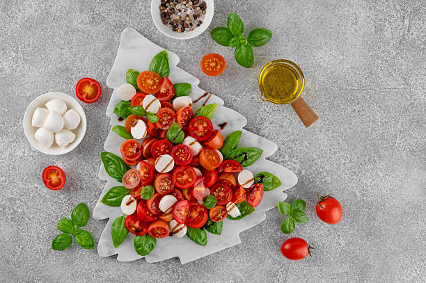 istock Festive Christmas Caprese salad with cherry tomatoes, mini mozzarella, and fresh basil served on a marble board, styled in the shape of a Christmas tree for holiday celebrations. Top view. 2249701859