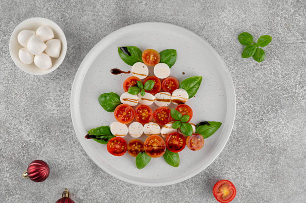 istock Festive Christmas Caprese salad with cherry tomatoes, mini mozzarella, and fresh basil served on a plate, styled in the shape of a Christmas tree for holiday celebrations. Top view. 2249701906