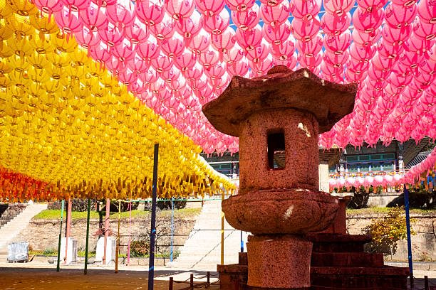 Gyeongsang, South Korea November 11, 2025. Stone lantern standing in temple courtyard decorated with vibrant pink and yellow paper lanterns for celebration in South Korea