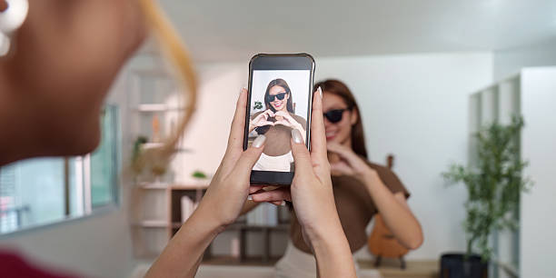 istock Creative Capture. Young woman posing for a smartphone photo while making a heart gesture. 2249706234