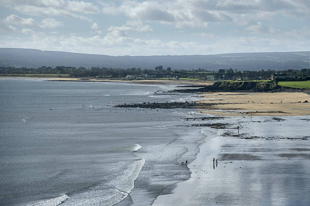 istock Panoramic high-angle of Irish coastline at Knock Bay Beach with wet sand reflections, distant hills, tidal surf, and silhouettes of people playing. 2249708721