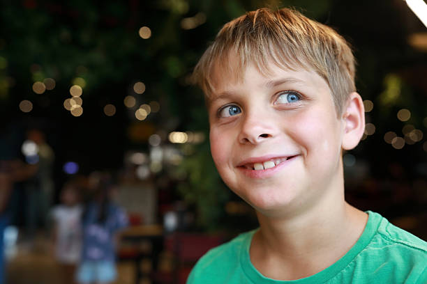 Happy young boy looking away with a smile, showing childhood joy and wonder. Playful kid in a restaurant or cafe, light bokeh background.