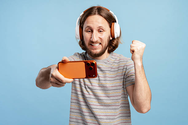 istock Excited man playing mobile game with headphones, celebrating victory 2249711877