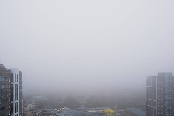Urban skyline on a foggy morning with high rise residential buildings and low visibility, city disappearing into dense mist creating moody atmospheric weather scene