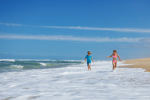 istock Kids boy and girl splashing through waves on bright beach day 2249712921