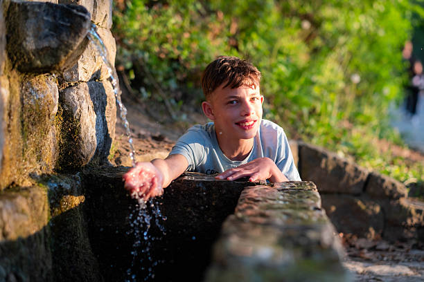 Boy smiling, enjoying splashing clean water from an old stone fountain in a park