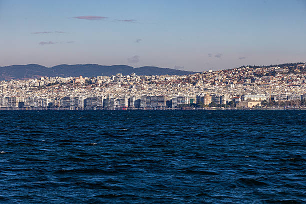 Thessaloniki, Greece – 30 November 2025: A wide coastal panorama of Thessaloniki with the dense urban hillside and the iconic White Tower visible along the seafront. The winter light highlights the continuous belt of waterfront buildings facing the Thermaic Gulf.