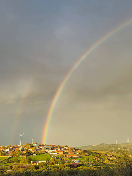 A Brilliant Double Rainbow Arcing Over a Sunlit Hillside Village After the Storm