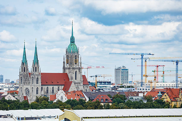 A scenic view of a historic St. Paul cathedral with green spires set against a backdrop of cranes, Munich, Germany