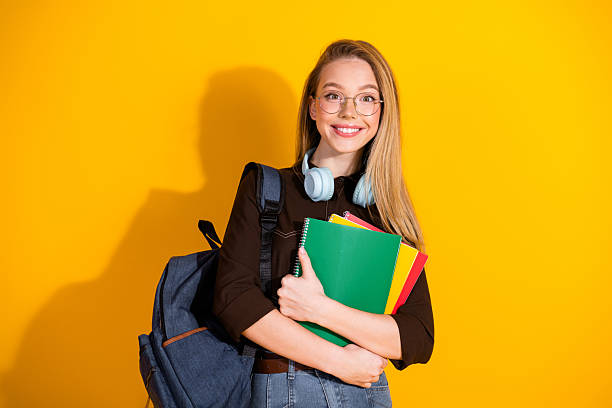 istock Young female student with backpack and colorful notebooks standing against a bright yellow background smiling 2249714500