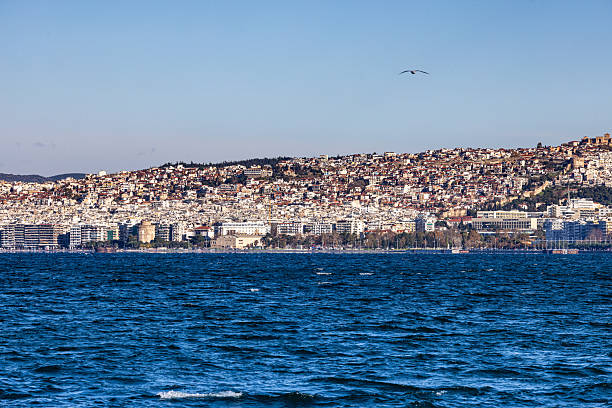 Thessaloniki, Greece – 30 November 2025: Panoramic view of the coastal skyline of Thessaloniki from across the Thermaic Gulf, featuring the White Tower and densely built urban neighborhoods rising up the hillside under clear winter light.