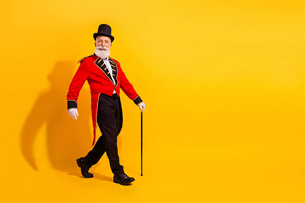 istock Circus showman in red coat and top hat striding across a bright yellow studio background 2249716961