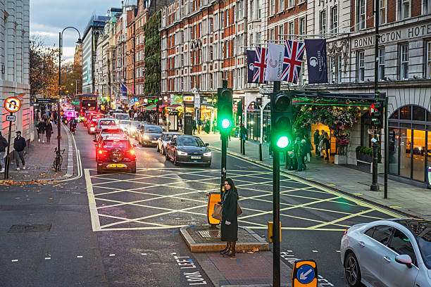 Southampton Row, London, England, United Kingdom, Europe - November 8th 2025: Pedestrian waiting for the green light at a hatched area on the road on a dark autumn afternoon during rush hour in central London.