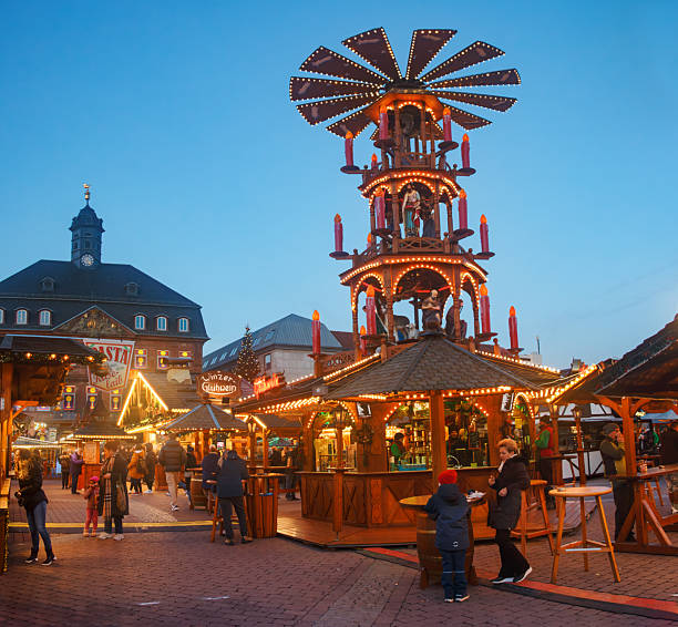 Christmas market with a beautiful and large Christmas pyramid is set up in the market square of Hanau, with the town hall in the background. The town hall windows are decorated and illuminated like an Advent calendar. The Christmas market in Hanau, Hesse, Germany, is open from November 24th to December 22nd.