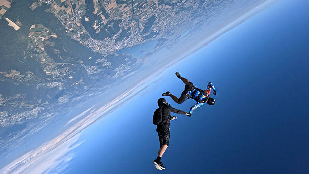Freefall jumpers hold hands upside-down mid-air above clouds and snowcapped Swiss Alps