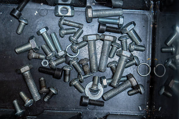 Top view of assorted metal bolts, screws, nuts and washers scattered inside a dark industrial storage box.