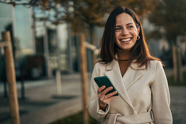 istock Woman smiling holding phone outdoors during autumn 2249729378