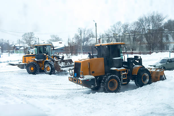 istock Two powerful snowplows work together to clear deep snow from residential street during heavy winter snowfall. Snow-covered houses and bare trees line the background, maintenance outdoors 2249729794