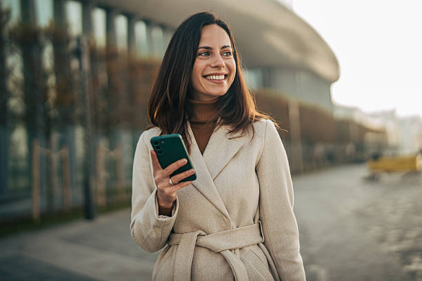 istock Young adult woman smiling while using smartphone in city 2249729969