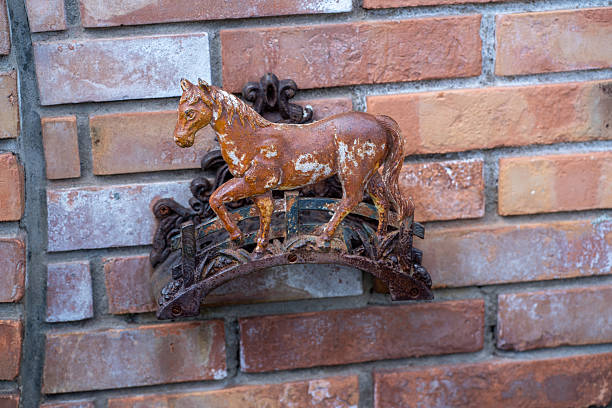 Close-up of a vintage rusty metal horse ornament mounted on an old brick wall, showing weathered texture, peeling paint and decorative wrought-iron details.