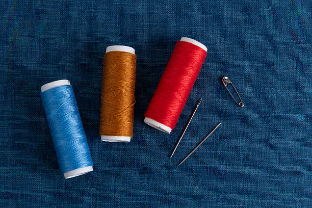 Colorful threads and needles on blue linen fabric