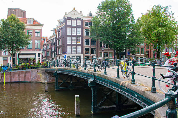 Amsterdam, Netherlands - 5 August 2025: Bicycles line the railings of a quaint bridge over a peaceful canal in the city.