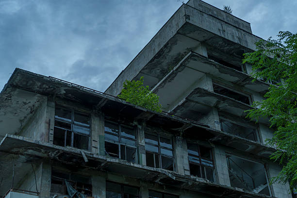 Decayed multi storey facade with broken windows and balconies stands bleak beneath a brooding cloudy sky.