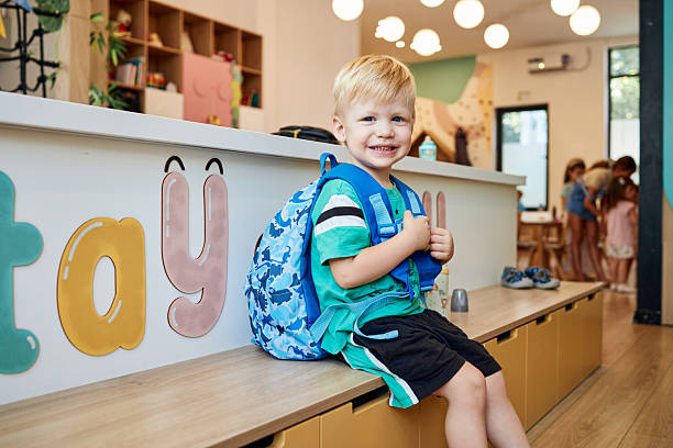 Happy child sitting on bench with his backpack in a kindergarten classroom