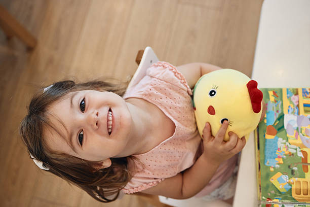 Child smiling, holding a plush chicken toy and an open book during playtime
