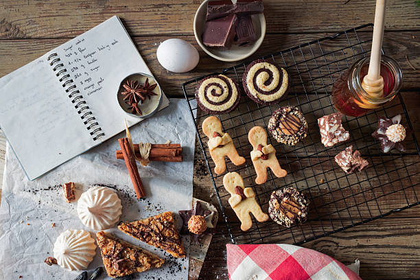 A top-down scene of festive cookies, meringues, and chocolate treats arranged around a handwritten sugar cookie recipe. A honey jar, cinnamon sticks, star anise, and a cracked egg create a nostalgic and sustainable holiday feel. Ideal for showcasing slow food, traditional baking, or zero-waste Christmas content. Ample room for copy and overlays.
