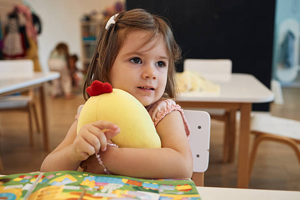 Happy little girl embracing her plush toy while learning in a classroom