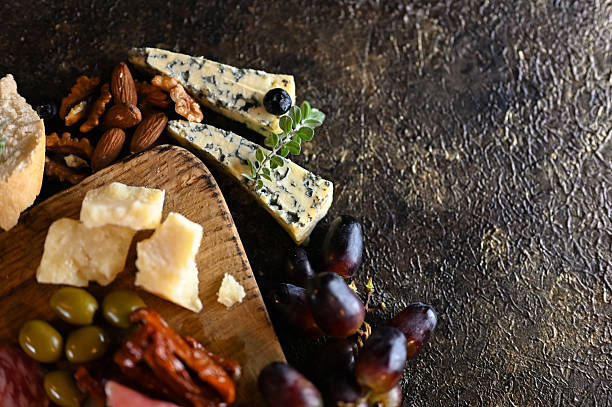Cheese board offering blue cheese, parmesan, grapes, nuts, olives, and charcuterie on dark background