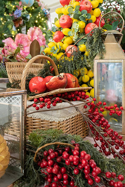 A vibrant holiday table featuring wicker baskets of apples, pomegranates, and citrus, accented by lanterns, greenery, and red berries.