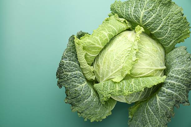 istock One fresh Savoy cabbage on green background, top view. Space for text 2249756955