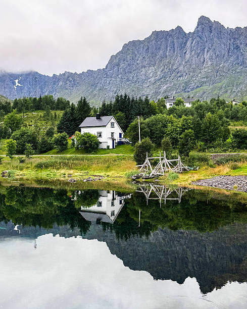 This is Northern Norway scenery. There is one house middle of nature and mountains. Northern Norway is known for its dramatic nature: towering fjords, rugged mountains, Arctic tundra, and vast coastlines. In summer, the Midnight Sun keeps the landscape bright around the clock, while in winter the region offers clear, dark skies perfect for seeing the Northern Lights. In this picture the reflection from the water is perfect.