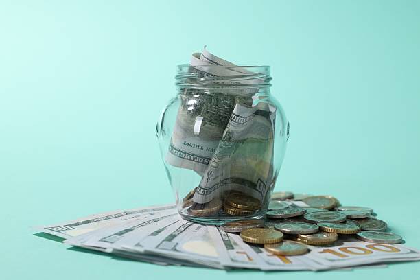 istock Glass jar with dollars and coins on light blue background, closeup 2249758223