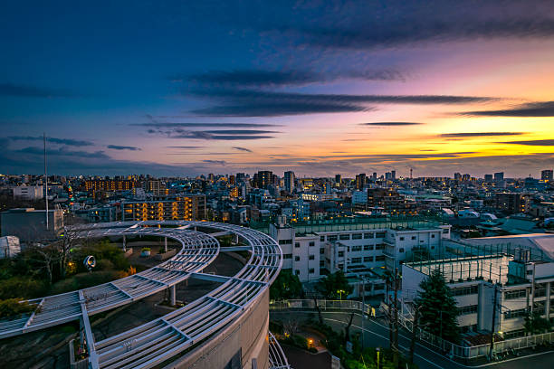 A vibrant twilight descends upon a sprawling cityscape, where dramatic streaks of purple and gold ignite the horizon. Below, the sleek, architectural curve of a modern structure overlooks the illuminated urban expanse, painting a scene of serene transition.