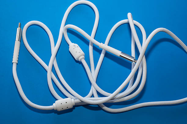istock ​A long, white audio cable in a protective fabric wrapping is coiled randomly on a bright blue background. Metal plugs are visible on both ends of the cable, along with plastic adjusters for length management. 2249759004