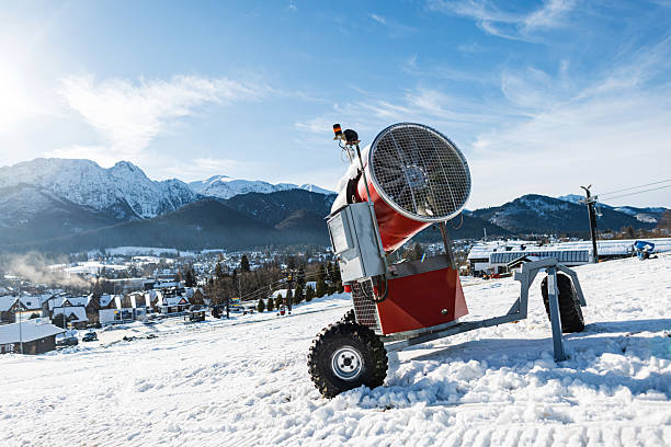 powerful, red mobile snow cannon sits on a bright, snow-covered ski slope with a stunning backdrop of the Tatra Mountains and a picturesque resort village. scene is captured on a clear, sunny winter