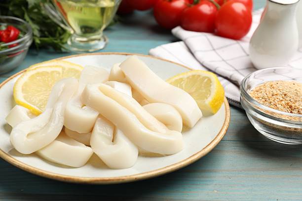 istock Raw squid rings, lemon and spices on light blue wooden table, closeup 2249761024