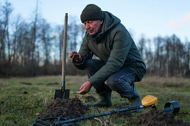 istock A man crouches in a grassy field, digging with a shovel as he inspects the ground for hidden treasures. The scene features a chilly autumn sky 2249764576