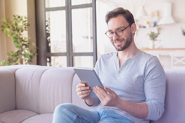 istock Confident young caucasian man using digital tablet sitting on the sofa, relaxing and reading e-book, e-learning, checking social media, doing online shopping, have zoom call conference at home indoors 2249765862