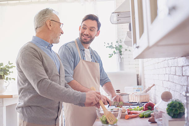 istock Happy young caucasian son talking with his old elderly senior father while cooking dinner, lunch in the kitchen. Preparing food meal together. Happy father`s day! I love you, dad! Men cooking together 2249767535