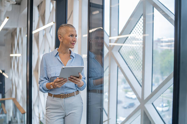istock Businesswoman holding digital tablet looking out modern office window 2249768069
