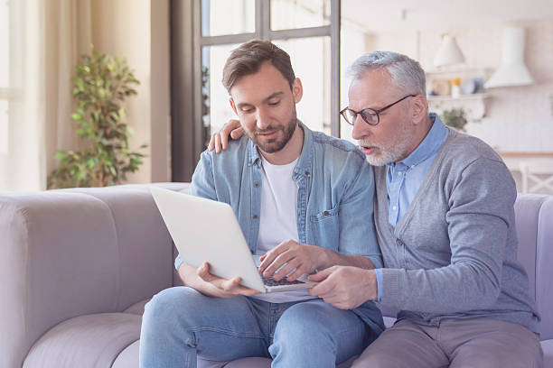 istock Helpful young adult son helping aiding his old senior elderly father in using laptop for watching movies, communicating online. Son teaching father how to use laptop. Happy father`s day! 2249769074